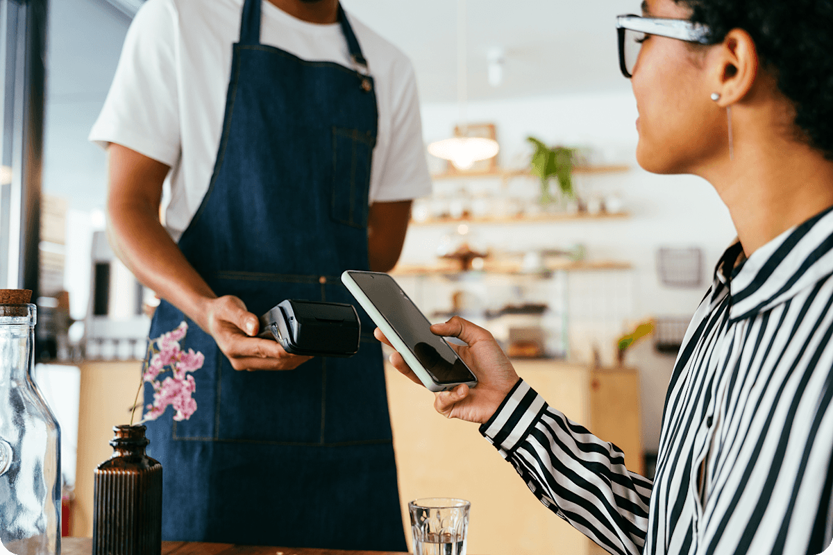 Eine Person in einem Café hält ihr Smartphone an ein Kartenlesegerät, um kontaktlos zu bezahlen.
